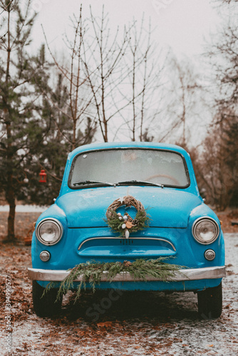 retro car decorated with festive Christmas tree branches, gift boxes craft wrapping paper wreath pine fir needles.
