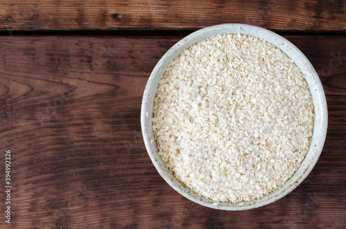 Squeezed white sesame in bowl on wooden background. Benne oilcake. Top view.