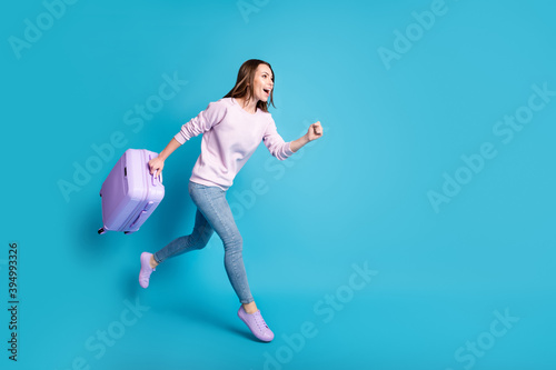Full size profile side photo cheerful crazy girl enjoy borders open hold suitcase jump run airport check-in travel wear lilac violet sweater denim jeans isolated blue color background