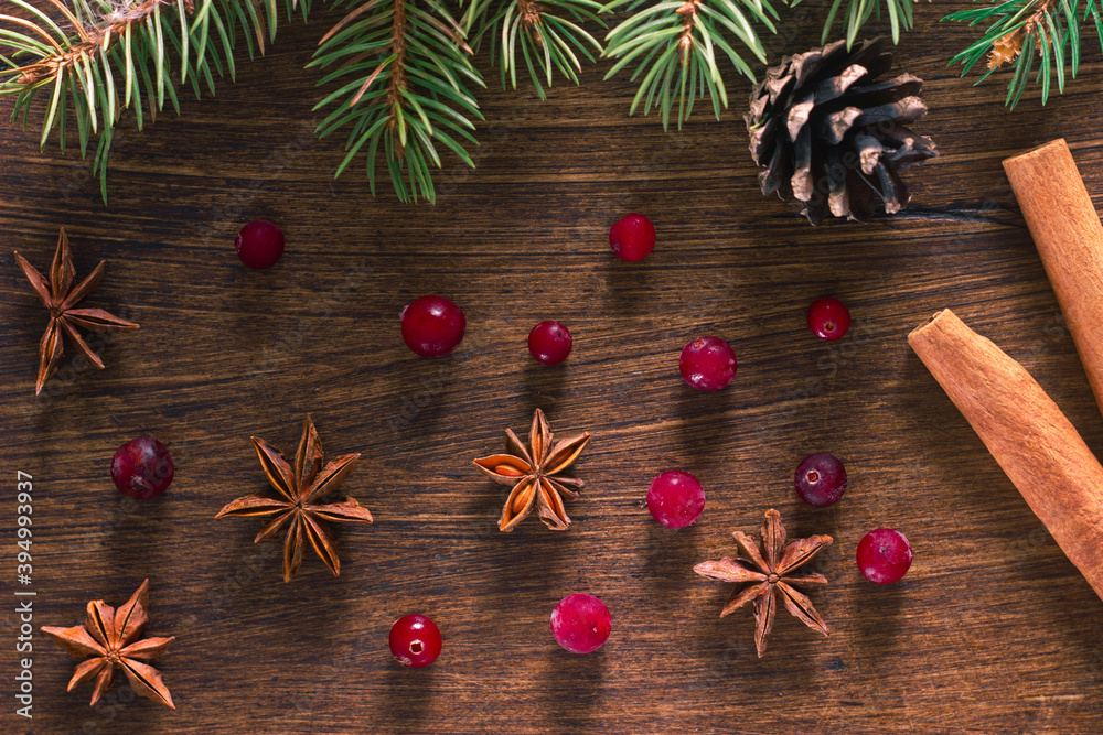 Christmas background: fur-tree branches, pine cones, cranberry, cinnamon sticks and anise stars on dark wooden background. Top view. Christmas decoration.