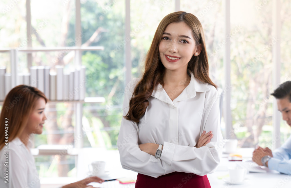 Young confident business woman standing in modern office. Portrait of young beautiful business woman in white in a busy modern workplace. Beautiful woman in office with business people. Young confident business woman standing in modern office. Portrait of young beautiful business woman in white in a busy modern workplace. Beautiful woman in office with business people.