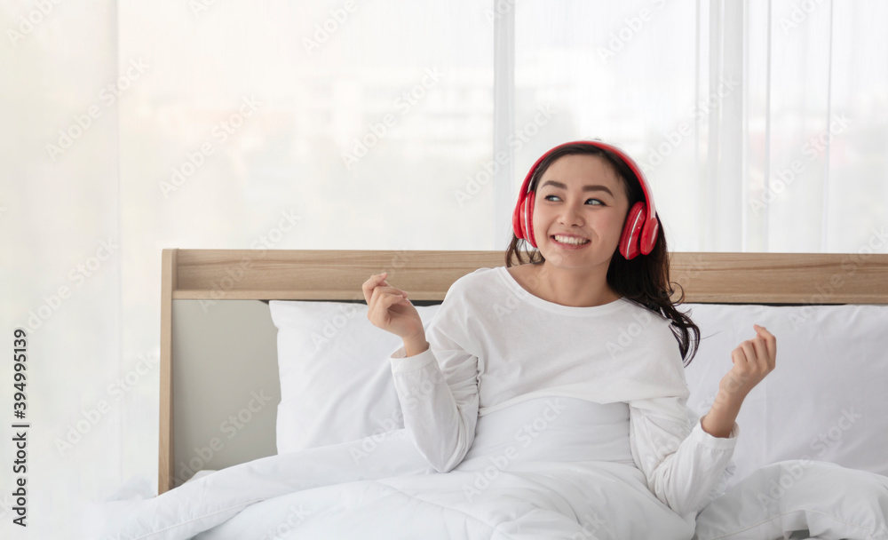 Happy young woman or teenage girl in headphones listening to music and dancing on bed at home. Young Girl listening music and dancing on bed. Beautiful young woman listening to music in headphones. Happy young woman or teenage girl in headphones listening to music and dancing on bed at home. Young Girl listening music and dancing on bed. Beautiful young woman listening to music in headphones.