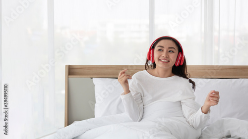 Happy young woman or teenage girl in headphones listening to music and dancing on bed at home. Young Girl listening music and dancing on bed. Beautiful young woman listening to music in headphones.