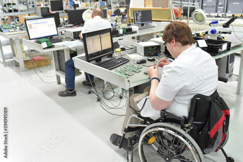 handicapped worker in a wheelchair at a workplace in a electronics manufacturing and assembly factory