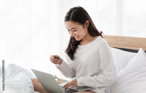 Young women doing online shopping on the bed. Woman shopping online with credit card and laptop computer while sitting on bed at home. Young girl using laptop computer at home online shopping.