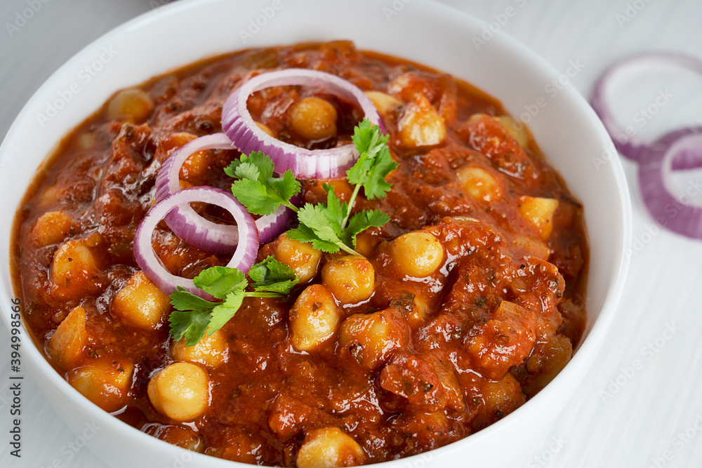 Closeup view of chole masala also known as channay, chana is an indian street food made of chickpeas, chopped tomatoes, ghee and cumin decorated with red onion rings and green parsley served in bowl Closeup view of chole masala also known as channay, chana is an indian street food made of chickpeas, chopped tomatoes, ghee and cumin decorated with red onion rings and green parsley served in bowl