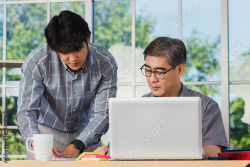 Asian senior and junior two businessmen discuss something during their meeting consultation project, Mature boss with a business partner working together on the laptop computer on desk home office