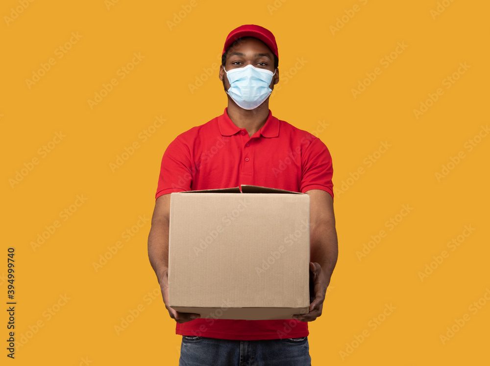 Black delivery man in medical mask giving box Black delivery man in medical mask giving box