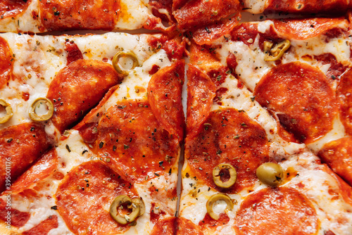 Pizza with pepperoni, cheese, tomatoes and olives on a light background close up, top view