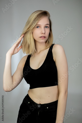 Portrait of a casual blonde woman in black top and jeans on gray background, ironing hair