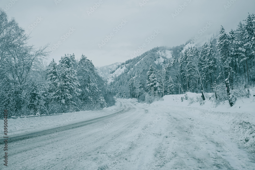 Winter landscape with a mountain road in the snow between mountains and a fir forest. Road drifts, snow. Winter's tale