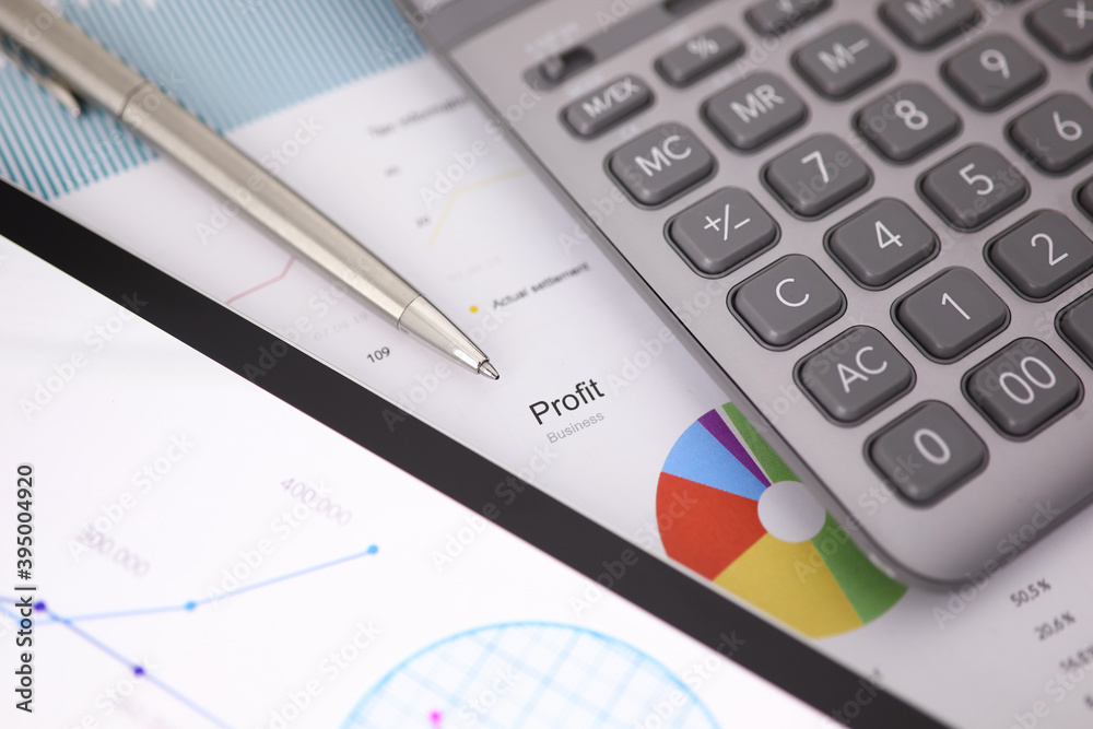 Siver pen calculator and tablet pc lie on office table against business chart closeup Siver pen calculator and tablet pc lie on office table against business chart closeup