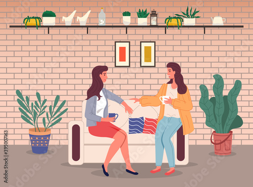 Brunette women girls sitting at sofa and talking. Friends relaxing with cup of tea or coffee. Happy girls spending leisure time at home. Sisters talking, relaxing at couch sofa in stylish living room