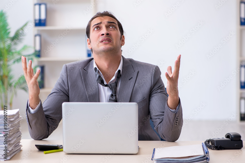 Young male employee unhappy with excessive work in the office Young male employee unhappy with excessive work in the office
