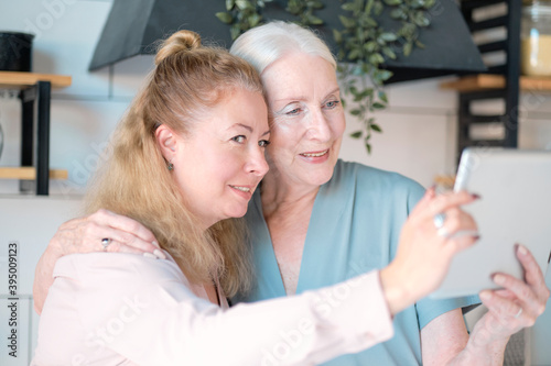 old mom and middle-aged daughter take selfies and talk via video link. Senior woman with her daughter looking at modern gadget indoors. relaxing together, different generations hobby pastime.