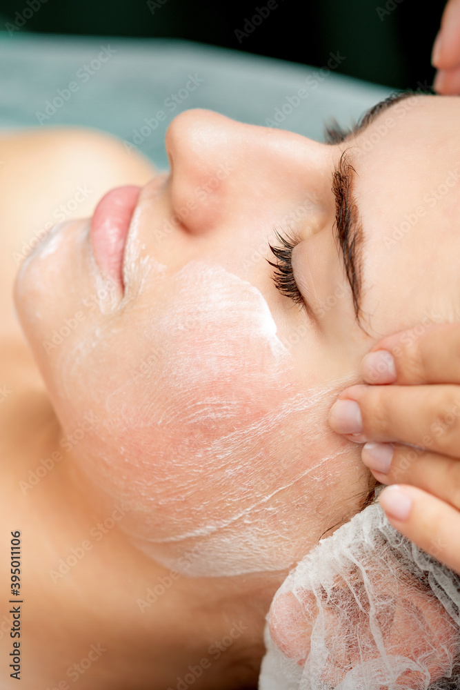 Fototapeta premium Young woman getting facial massage with closed eyes by beautician in beauty salon