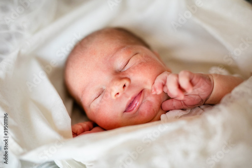 Newborn baby for the first time at home, lying in a blanket on the bed, smiling, yawning, pulling pens, falling asleep, baby's morning, baby products concept.