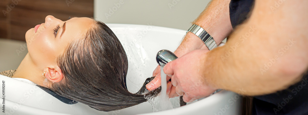 Fototapeta premium Male hairdresser rinses hair of young woman after shampooing at hair salon