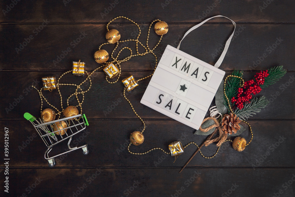 Xmass Sale word on lightbox and small shopping cart with golden gifts on wooden background