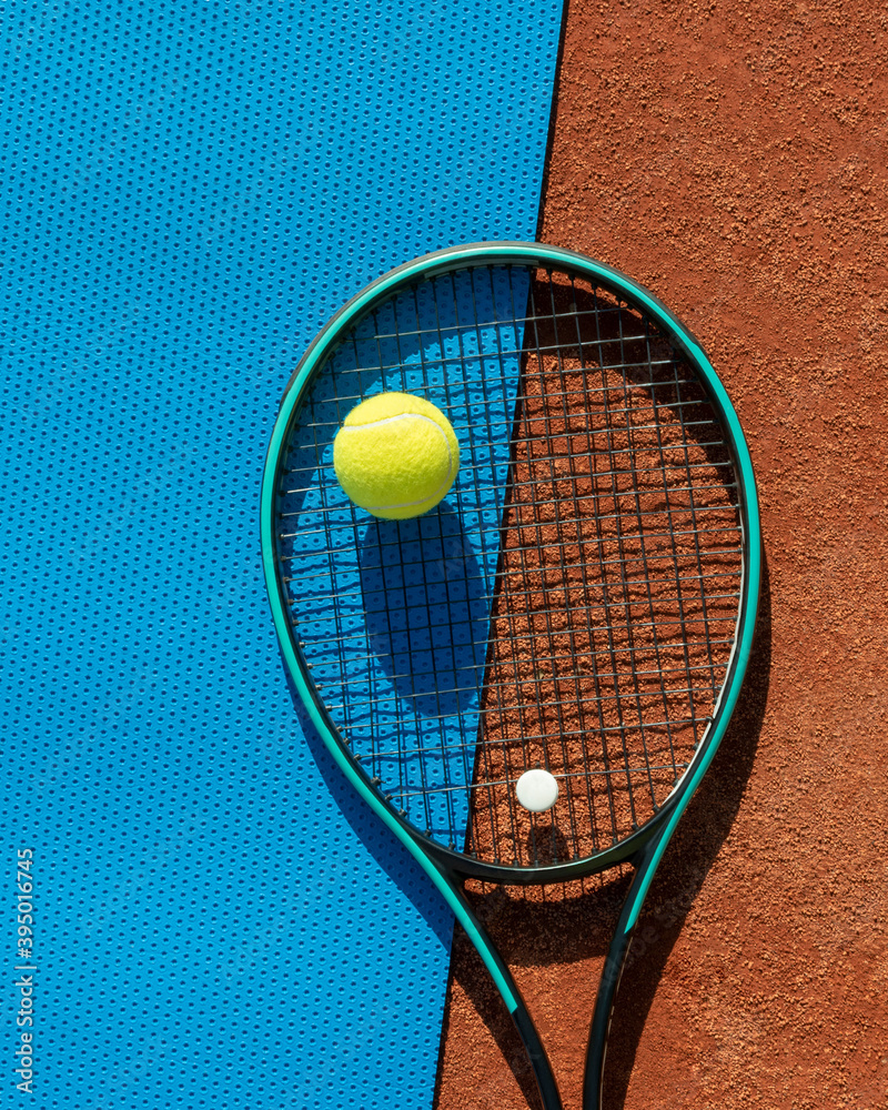 Tennis racket and balls on red clay court and blue gym mat. Sport tennis, active games, leisure and healthy lifestyle. Sports background. Vertical. Copy space