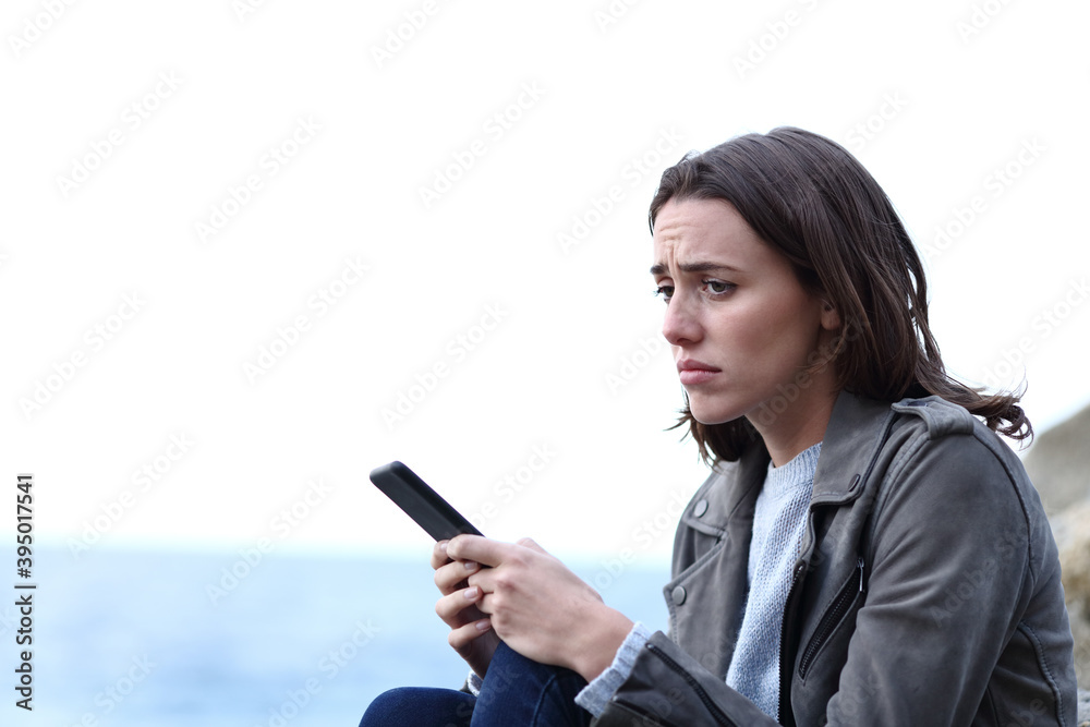 Sad woman holding phone complaining on the beach Sad woman holding phone complaining on the beach
