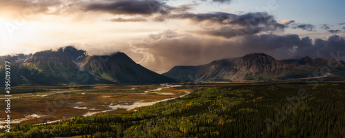 Beautiful Panoramic View of Lush Forests  Trees and Land surrounded by Mountains in Canadian Nature. Dramatic Colorful Sunset Sky. Aerial Drone Shot. Taken near Alaska Highway  Yukon  Canada.