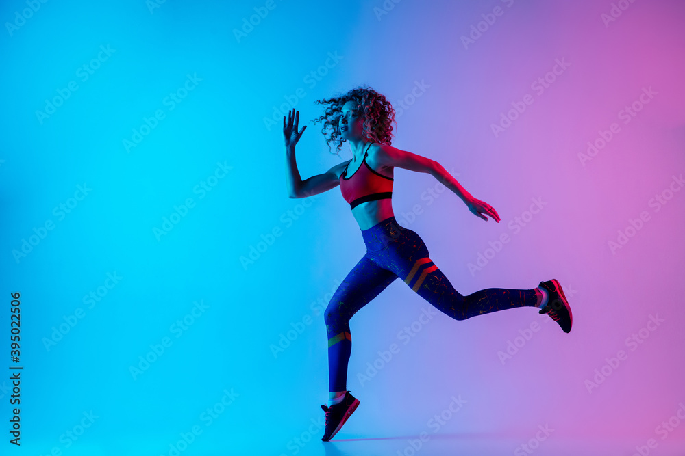 Runner. Young sportive woman training isolated on gradient blue-pink studio background in neon light. athletic and graceful. Modern sport, action, motion, youth concept. Beautiful female practicing.