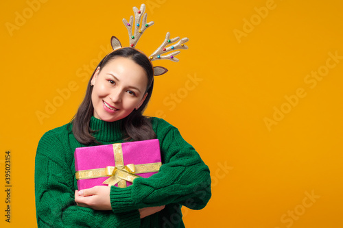 happy young woman with christmas deer antlers with gift on yellow background