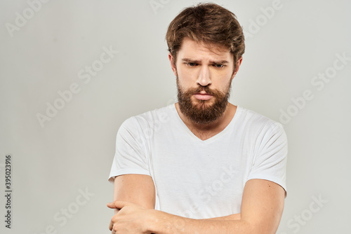 A man in a white t-shirt with a beard emotions displeased facial expression light background