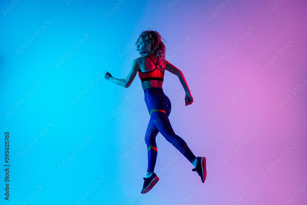 Runner. Young sportive woman training isolated on gradient blue-pink studio background in neon light. athletic and graceful. Modern sport, action, motion, youth concept. Beautiful female practicing.