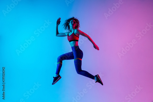 High jump. Beautiful woman in bright sportwear isolated on gradient pink-blue background in neon light. Athletic and graceful. Modern sport, action, motion, youth concept. Sportive female practicing © master1305