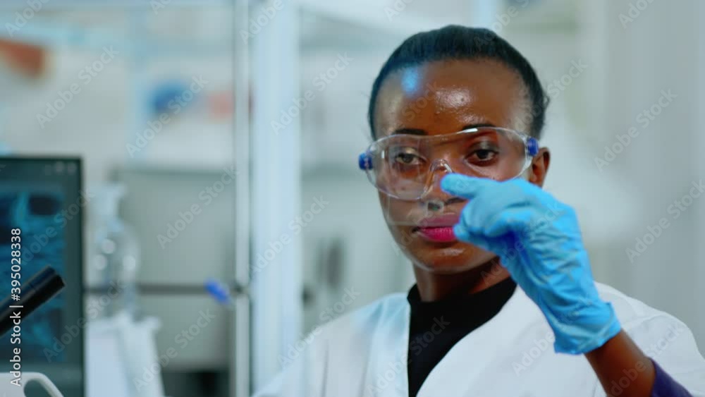 Close up of african chemist looking at virus test in equipped lab. African scientist working with various bacteria, tissue and blood samples, concept of pharmaceutical research for antibiotics. Close up of african chemist looking at virus test in equipped lab. African scientist working with various bacteria, tissue and blood samples, concept of pharmaceutical research for antibiotics.