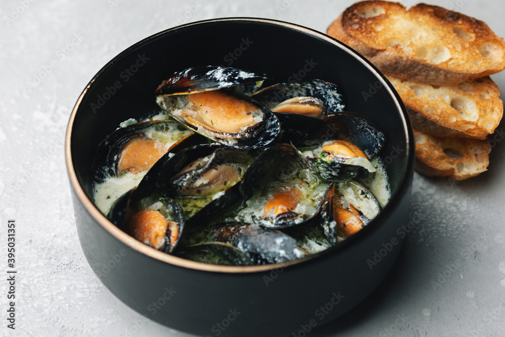 Cooked mussels with cream and white wine sauce, roasted toasts. Mediterranean cuisine. Concept for a tasty and healthy meal. Close up. Selective focus Cooked mussels with cream and white wine sauce, roasted toasts. Mediterranean cuisine. Concept for a tasty and healthy meal. Close up. Selective focus