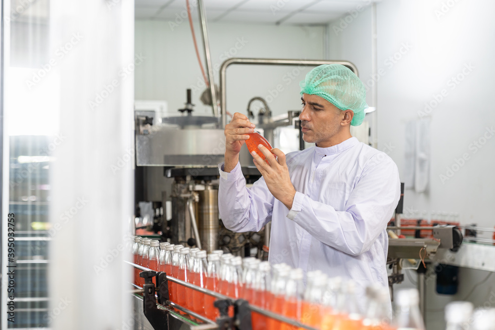 Naklejka premium Male specialist checking goods or product bottles. Male worker checking product of Basil seed with fruit on the conveyor belt in the beverage factory before shipment. Inspection quality control
