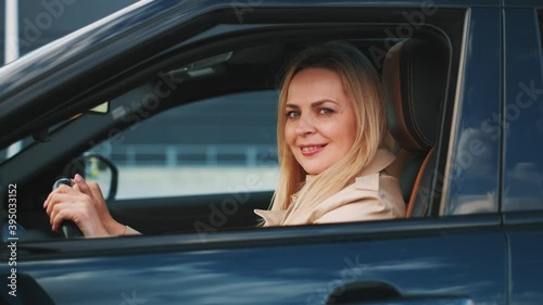 The woman is sitting behinde the wheel of the brandnew car. She is looking happy. photo