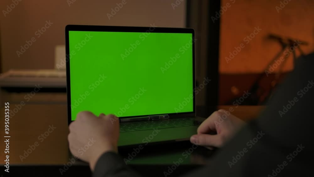 Faceless male making online call via laptop webcam with chromakeyed display. Green screen for tracking copy space. Display replacement of on-line conference indoor of cozy home interior. Faceless male making online call via laptop webcam with chromakeyed display. Green screen for tracking copy space. Display replacement of on-line conference indoor of cozy home interior.