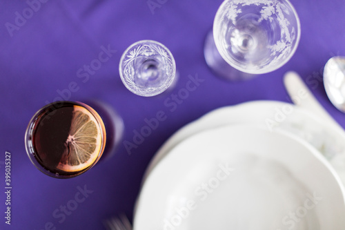 Two empty glasses and plates with one full glass of lemonade with lemon on a purple tablecloth