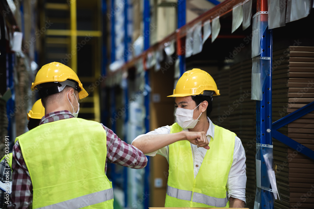 Diverse males warehouse colleague wear face mask, keeping social distancing and greeting by touching elbows instead of hugs or handshaking to prevent COVID-19 infection. Greeting in New normal style. Diverse males warehouse colleague wear face mask, keeping social distancing and greeting by touching elbows instead of hugs or handshaking to prevent COVID-19 infection. Greeting in New normal style.