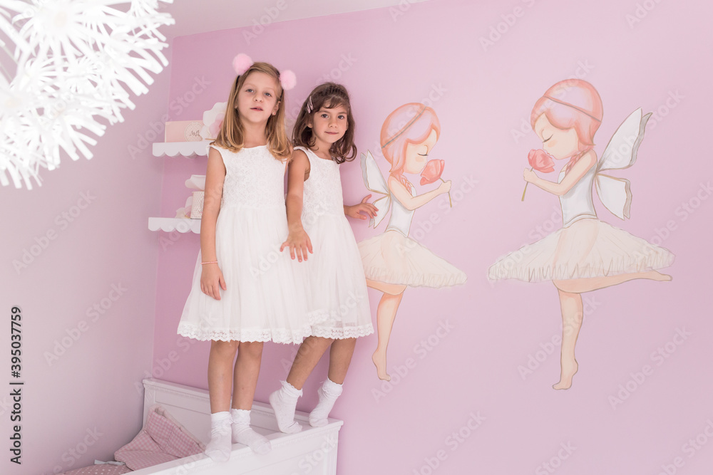 Cute, little girls, sisters, twins standing on the bed in their lovely pink room Cute, little girls, sisters, twins standing on the bed in their lovely pink room