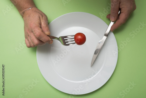 Closeup of hands of woman eating one cherry tomato in her white plate on green background - Dieting concept