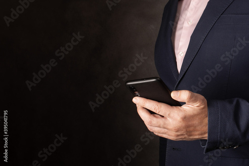 Businessman using mobile cell phone app texting on dark background. man in suit holding smartphone for business work. copy space