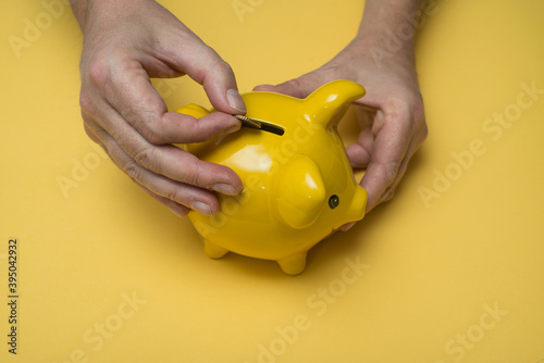 Closeup of hands of man insert one euro coin in his yellow piggy bank on yellow background