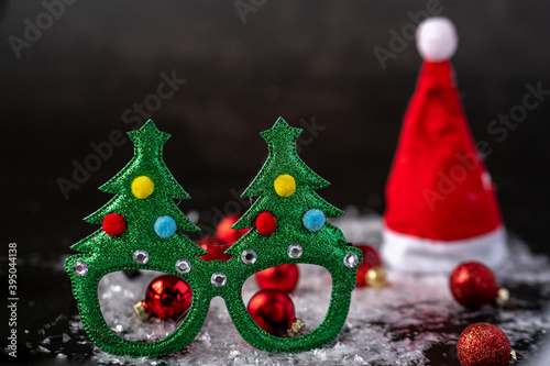 New Year's glasses with a green tree, decorated with New Year's toys, decor, lie on a table with snow and next to New Year's balls in red and a red cap with a bumbon photo