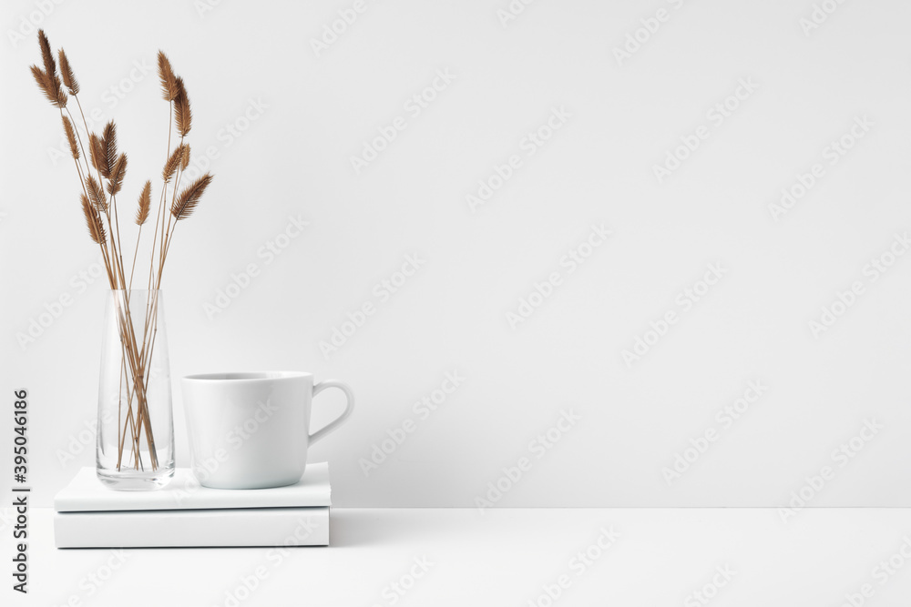Mug and transparent vase with flowers on a white background. Eco-friendly materials in the decor of the room, minimalism. Copy space, mock up - obrazy, fototapety, plakaty 