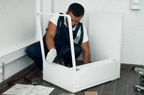 Furniture assembly process. Worker in overalls and white footwear. Joining pieces of furniture. Do it yourself.
