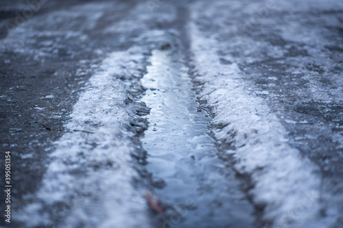 Frozen water in a puddle. Sunlight reflects off the frozen surface of the puddle. Natural phenomenon, abstract background.