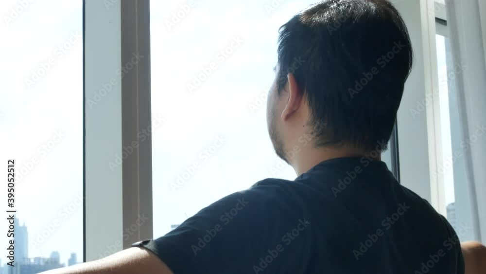a young man open curtain watching view throughout window with sunshine a young man open curtain watching view throughout window with sunshine