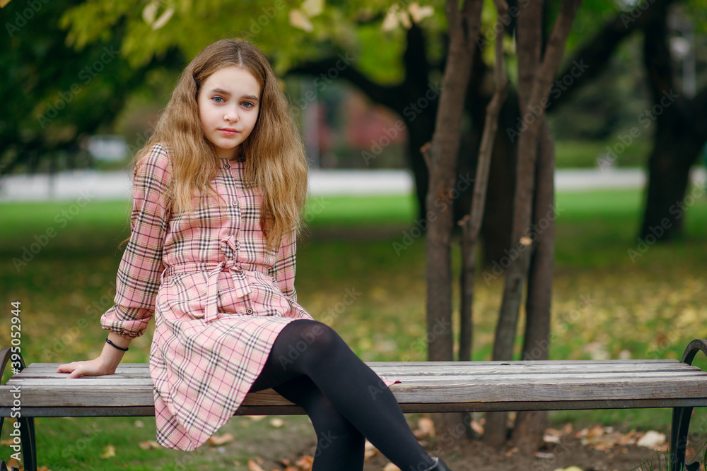A cute teenage girl with lush hair in a beautiful plaid dress sits on a park bench A cute teenage girl with lush hair in a beautiful plaid dress sits on a park bench