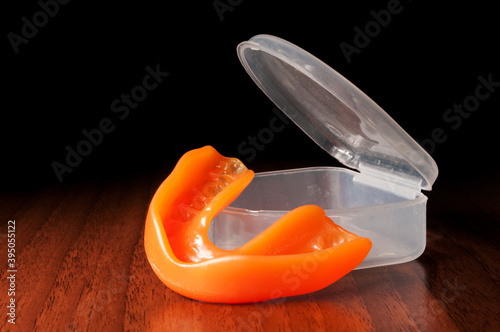 Orange mouthguard near opened case on the wooden texture and black background