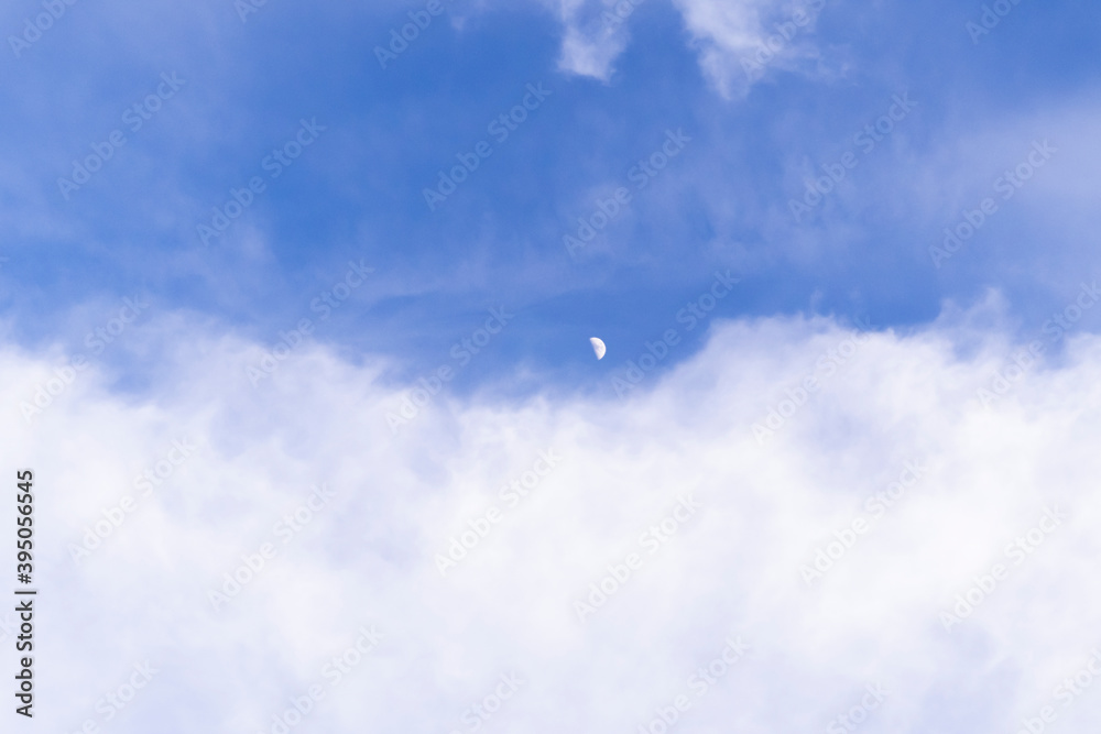 Blue bright sky with white clouds. Moon in daylight Blue bright sky with white clouds. Moon in daylight